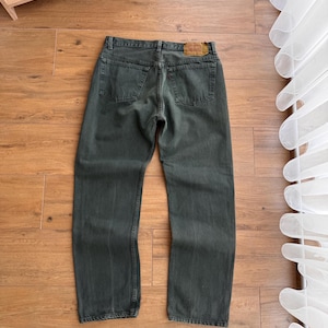 Op de afbeelding: Donkergroene denim jeans met een klassiek vijf-zakken ontwerp. De jeans heeft een rechte pijp en een leren patch op de achterste tailleband. De jeans ligt plat op een houten oppervlak.