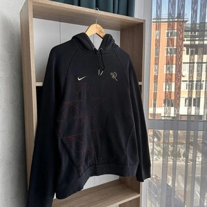 Op de afbeelding: Zwarte hoodie met een rood en wit sterrenontwerp en een Nike-logo op de linkerborst. De tekst "1/2" staat op de rechterborst.