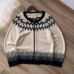 May include: Cream-colored zip-up sweater with a navy blue and gray geometric pattern. The sweater has a round neckline and long sleeves. The bottom and cuffs are navy blue. The brand name "KAREN" is visible on the label.