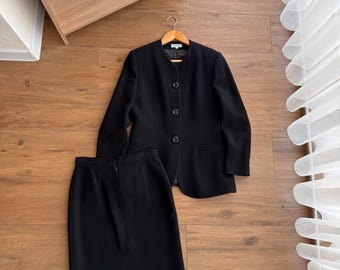 May include: A black skirt suit with a blazer and a knee-length skirt. The blazer has a round neckline and three buttons.
