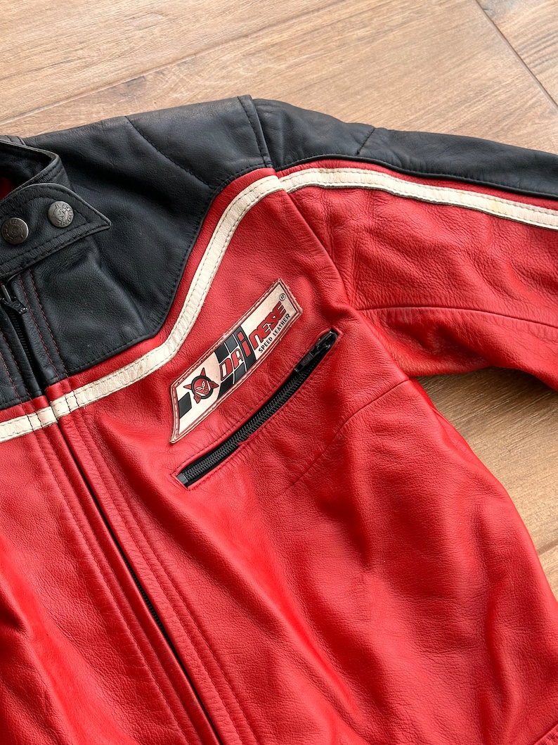 May include: Red leather motorcycle jacket with black and white racing stripes and a Dri-Mex Speed Leather patch on the left chest.