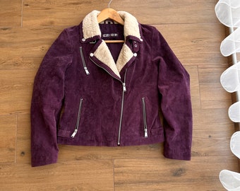 May include: A purple suede jacket with a faux fur collar and zipper closure. The jacket has multiple zipper pockets and a silver zipper pull.