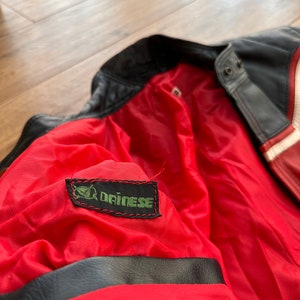 May include: Close-up of the red lining of a black leather jacket with a green Dainese logo patch.