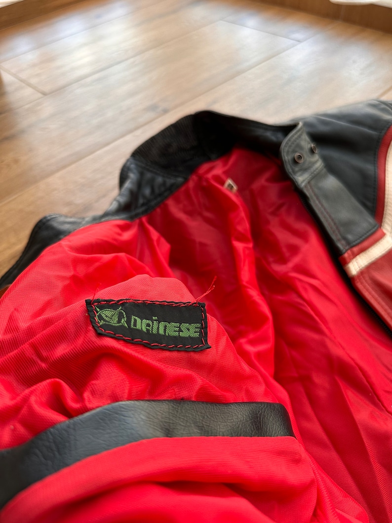 May include: Close-up of the red lining of a black leather jacket with a green Dainese logo patch.