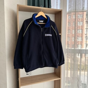 Puede incluir: Una chaqueta de forro polar azul marino con una cremallera amarilla y una raya amarilla en las mangas. La chaqueta tiene un forro polar azul y un logotipo de Michelin en el pecho.