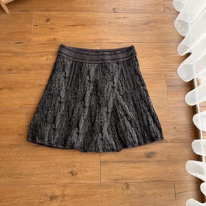 May include: A white ceramic mug with a black handle and the text "But First, Coffee" in a black, bold font. The mug is on a white surface.