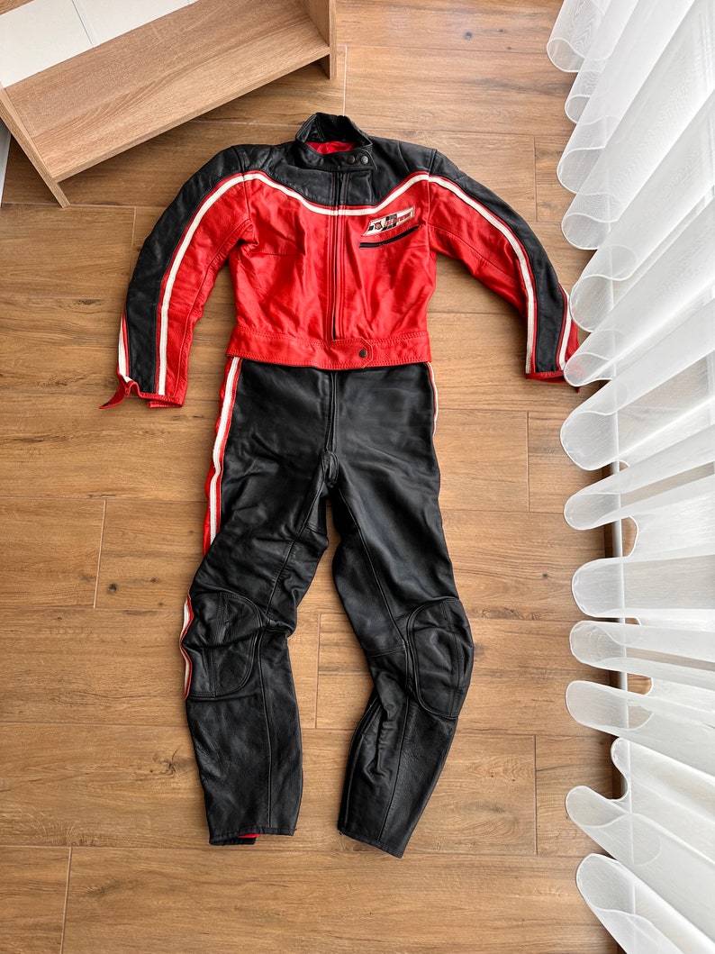 May include: A red and black leather motorcycle suit with white stripes. The jacket has a zipper closure and a patch on the left chest that says "No Fear".