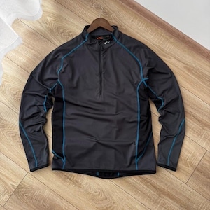 May include: A charcoal gray long-sleeve athletic top with a quarter-zip closure and a stand-up collar. The top features teal blue accent stitching along the seams and a small logo on the chest. The garment is displayed on a wooden hanger.