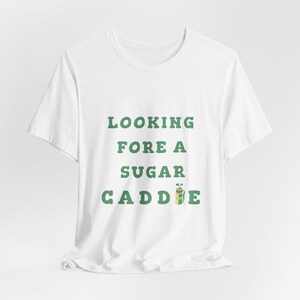May include: White t-shirt with green text that reads "Looking Fore A Sugar Caddie" with a green and brown golf bag icon.