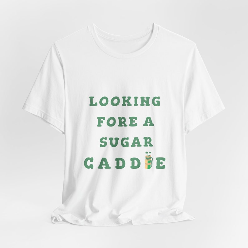 May include: White t-shirt with green text that reads "Looking Fore A Sugar Caddie" with a green and brown golf bag icon.