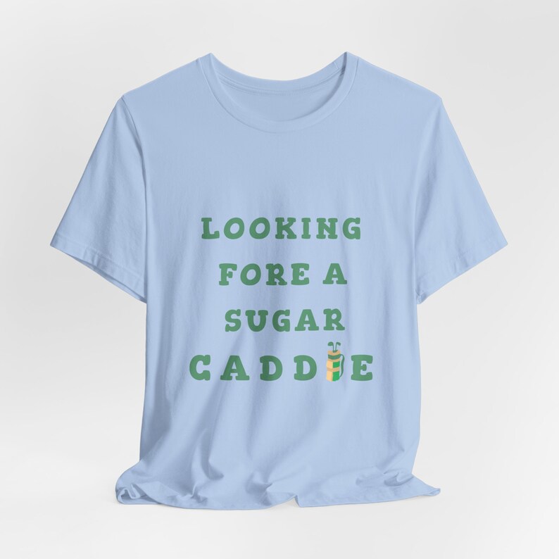 May include: Light blue t-shirt with the text "LOOKING FORE A SUGAR CADDIE" in green letters. A cartoon golf bag with a golf club is next to the text.