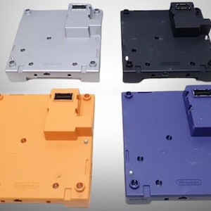 Puede incluir: Cuatro carcasas inferiores de consola Nintendo GameCube de colores: plateado, negro, naranja y morado. Cada carcasa tiene forma rectangular con una sección elevada y varios puertos.