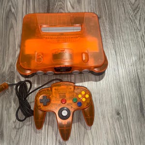 Consola Nintendo 64 naranja con todos los cables y un mando