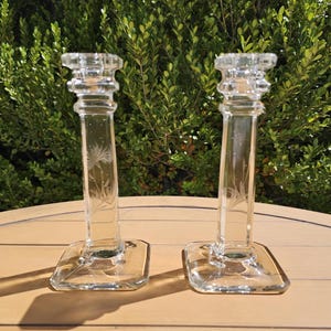 May include: A white ceramic mug with a black handle and the text "But First, Coffee" in a bold, black font. The mug is set against a blurred background, suggesting a cozy setting.