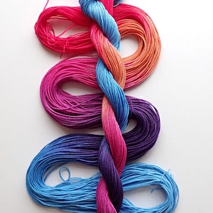 May include: A vibrant display of embroidery floss in shades of pink, orange, blue, and purple. The floss is arranged in a flowing, intertwined pattern, creating a visually appealing design. The image is well-lit, highlighting the colors and textures of the threads.