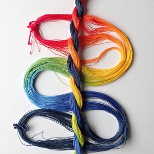 May include: A central vertical braid of multi-colored thread is flanked by three horizontal loops of thread on each side. The colors transition from dark blue at the top to red, orange, yellow, green, blue, and dark blue, ending in light blue.