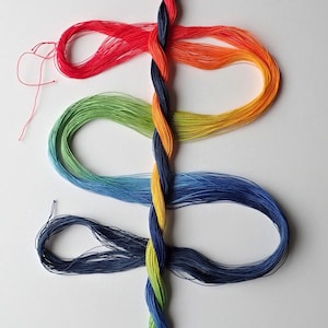 May include: A vertical braid of dark blue, orange, and yellow thread serves as a central spine, with loops of red, orange, yellow, green, blue, and dark blue thread extending horizontally from the braid, creating a colorful, layered arrangement.