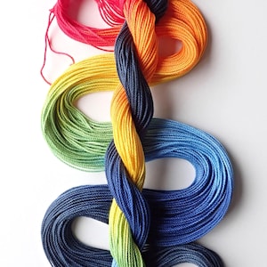 May include: A braided hank of embroidery thread featuring a vibrant gradient of colors including dark blue, bright red, orange, yellow, light green, and medium blue. The text Marilee Rockley yarnplayer.etsy.com is printed in the bottom right corner.