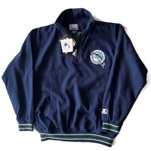 May include: A navy blue quarter-zip pullover sweatshirt with a green and white striped collar. The sweatshirt has a ribbed texture and features a Florida Marlins logo on the right chest and a Starter logo on the left sleeve.