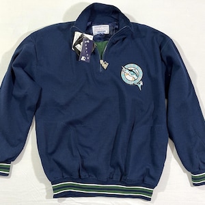 May include: A navy blue quarter-zip pullover sweatshirt with a green and white striped cuff and waistband. The sweatshirt features a green and white embroidered logo of a marlin fish on the left chest.
