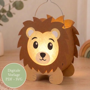 May include: A paper lantern shaped like a lion with a brown mane and a light-colored face. The lantern features a metal handle at the top and emits a warm glow from within. A circular green badge on the left displays the text Digitale Vorlage PDF + SVG.