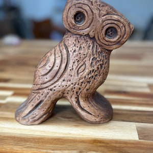 May include: A brown ceramic owl figurine with detailed carvings. The owl has large, round eyes and a textured surface.