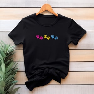 May include: Black t-shirt with five paw prints in a row. The paw prints are pink, yellow, and blue.