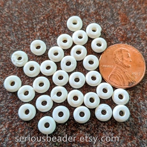 May include: A pile of 30 white plastic donut beads, approximately the size of a US penny. The beads have a smooth, matte finish and a hole in the center.