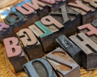 May include: A collection of vintage wooden letterpress printing blocks. The blocks feature individual letters in various colors, including pink, green, and red. The blocks are arranged on a textured, golden-yellow surface. The Etsy shop name "seriousbeader.etsy.com" is visible.