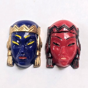 May include: Two vintage plastic masks with gold trim. The mask on the left is blue with yellow eyes and a red mouth. The mask on the right is red with black eyes and a red mouth.