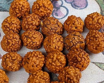 May include: A collection of approximately 20 brown, round beads with a textured surface. The beads are arranged in a loose pile on a white fabric with a floral pattern.