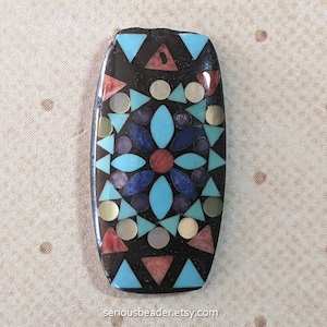 May include: A rectangular, mosaic-style pendant with a black background. The design features a central floral pattern in blue, red, and purple, surrounded by turquoise triangles, and iridescent and gold-colored circles. The text "seriousbeader.etsy.com" is at the bottom.