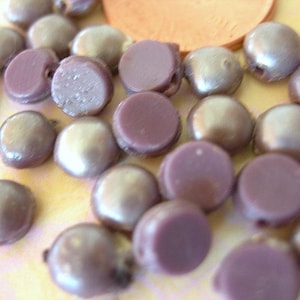 May include: A collection of round, iridescent purple and silver cabochons. The cabochons are smooth and have a slightly pearlescent finish.