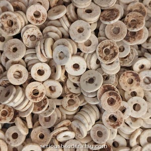 May include: A pile of off-white, donut-shaped beads with a central hole. Some beads have brown, speckled markings. The beads are arranged closely together, filling the frame. The Etsy shop name "seriousbeader.etsy.com" is visible in the bottom right corner.