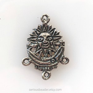 May include: Silver-toned metal charm featuring a sun face with a smiling expression. The sun is surrounded by rays and is set within a crescent moon shape. The charm has three loops for attaching to jewelry or other crafts.