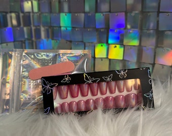 May include: A set of pink press-on nails with a holographic finish, packaged in a black box with butterfly designs. The box also includes a nail file.
