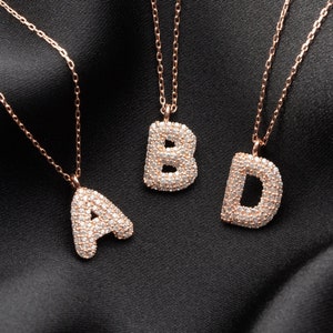 Könnte beinhalten: Drei goldene Halsketten mit diamantbesetzten Buchstabenanhängern. Die Buchstaben sind A, B und D.