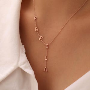May include: A delicate rose gold necklace spelling out the name "PAMELA" in individual capital letters. The letters are connected by a fine chain, with the final "A" hanging vertically. The necklace is displayed against a white background.