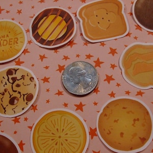 Op de afbeelding: Een verzameling van 10 ronde, kleurrijke papieren stickers met verschillende ontwerpen. De stickers bevatten afbeeldingen van koekjes, een munt en een sticker met tekst die zegt "Ik ben een leider".