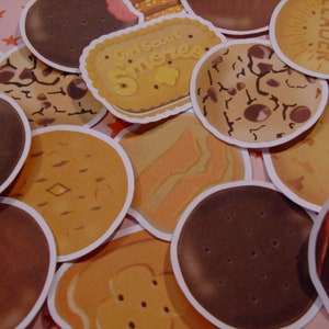 Op de afbeelding: Een verzameling ronde, kleurrijke en gepatroneerde koekjestickers. De stickers hebben verschillende ontwerpen, waaronder een Girl Scout S'mores-koekje, een chocoladekoekje en een pindakaaskoekje.