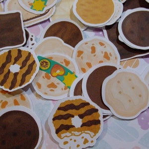 Pu&ograve; includere: Assortimento di adesivi per biscotti illustrati e colorati. Gli adesivi presentano diversi design, tra cui biscotti al cioccolato, biscotti secchi e biscotti al burro di arachidi.