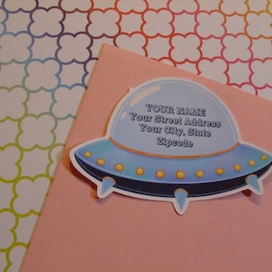 May include: A blue and white UFO-shaped sticker with the text "YOUR NAME", "Your Street Address", "Your City, State", and "Zipcode".