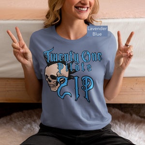 Könnte beinhalten: Lavendelblaues T-Shirt mit dem Text "Twenty One Pilots" und einer Totenkopf-Grafik in Blau und Schwarz. Das T-Shirt hat einen Rundhalsausschnitt.