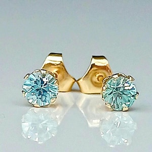 May include: A pair of gold stud earrings with light blue round gemstones.
