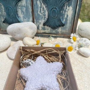 May include: A white crocheted star keychain with a black and white polka dot ribbon attached to a silver key ring. The keychain is in a small brown box with shredded paper.