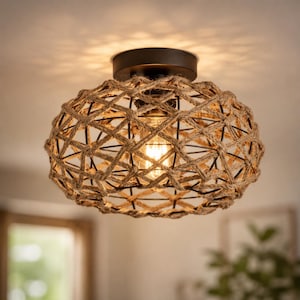 Pode incluir: Uma luminária de teto embutida com base de metal marrom escuro e uma estrutura de gaiola esférica envolta em corda de juta grossa de cor castanho natural. O design de trama aberta permite a passagem da luz, criando um brilho estampado.