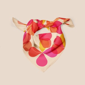 May include: A cream-colored silk scarf with a geometric pattern of overlapping pink, red, and yellow circles.