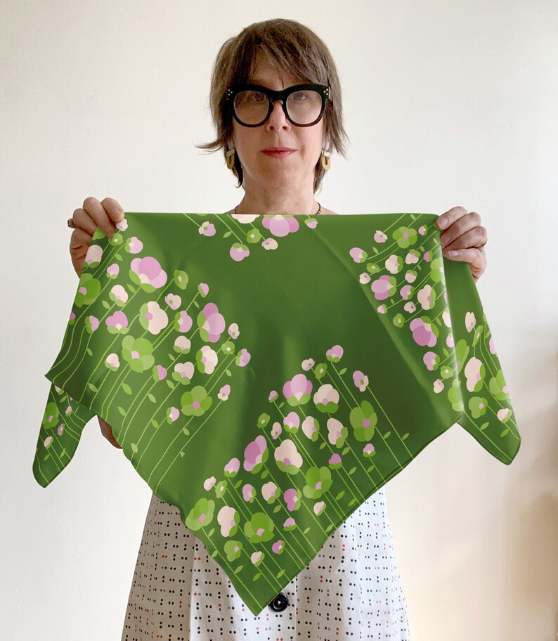 May include: A green silk scarf with a pink and green floral pattern. The scarf is folded in half and held by a person wearing glasses.