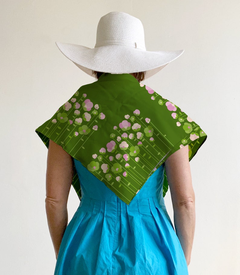 May include: A woman wearing a white sun hat and a green scarf with pink and green floral print. The scarf is tied around her neck and drapes down her back. She is wearing a bright blue dress.