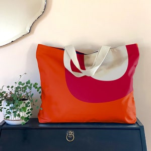 May include: Orange and red tote bag with white canvas straps. The bag has a geometric design with a large red semi-circle on the front.